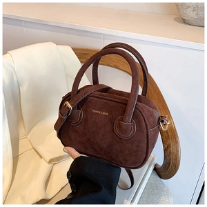 Détail du sac Boston en daim marron foncé avec inscription dorée sur un siège en bois