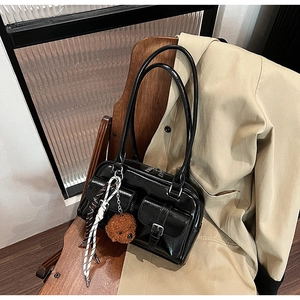 Détail d'un sac à bandoulière en cuir verni noir avec poches et charm ours peluche