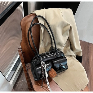 Détail d'un sac d'épaule en cuir verni noir brillant avec poches et charm d'ours