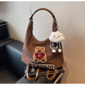 Dettaglio borsa hobo marrone con ricamo a forma di orso e ciondolo in peluche sul divano