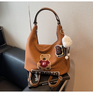 Dettaglio della borsa hobo marrone caramello con patch orso e ciondolo nuvola