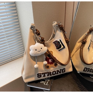 Dettaglio borsa tote beige vintage con manici intrecciati e toppe in stile varsity