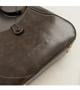 Detail of vintage brown leather bag with embossed logo and contrast white stitching