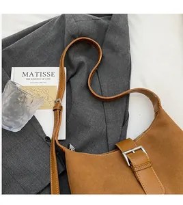 Detail of caramel suede crescent shoulder bag with buckle strap on a grey blazer