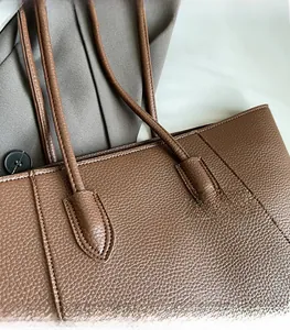 Close-up of reinforced stitching and lychee grain leather on a brown tote bag