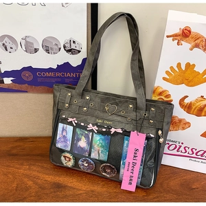 Detail of grey oxford ita bag with transparent window featuring anime pins and pink bow