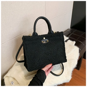 Detail of plush black tote bag featuring golden oval clasp and leather handles