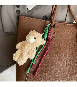 Close-up of a teddy bear plush charm with woven rope on a brown leather tote bag