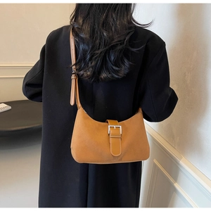 Detail view of a tan leather hobo bag with silver buckle worn over a black winter coat