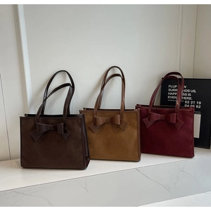 Detailed view of three suede tote bags in coffee, camel and burgundy with bows