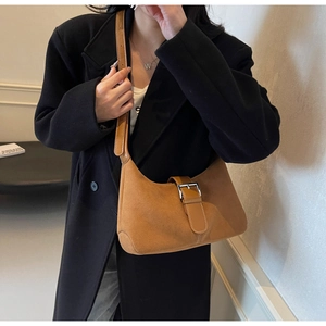 Detail of a brown suede shoulder bag with a silver buckle worn over a black coat