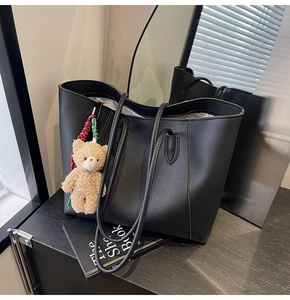 Detail of a black pebbled faux leather tote bag with a cute brown plush bear charm