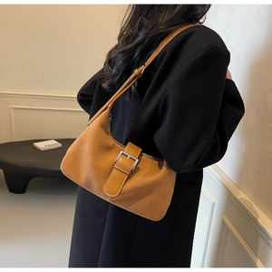 Brown suede crescent bag with silver buckle detail shown on a person's shoulder