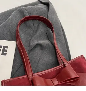 Detailed view of burgundy suede tote bag featuring a large decorative bow and mixed textures