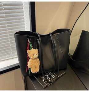 Detail of black pebbled leather tote with plush bear charm in natural light
