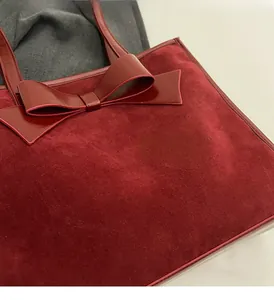Close-up of burgundy suede tote bag featuring a large decorative leather bow detail