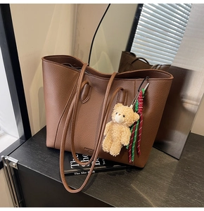Brown lychee leather tote bag featuring a plush bear charm and contrast tassel decoration