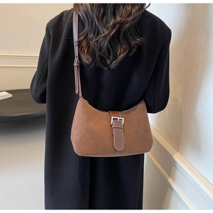 Detail of a brown suede crescent bag featuring leather strap and metallic buckle design
