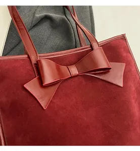 Detailed view of burgundy suede tote bag featuring a large glossy leather bow decoration