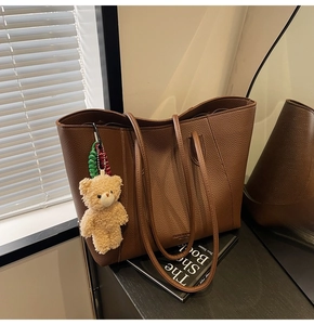Detail of brown litchi pattern tote bag featuring a cute plush bear charm accessory