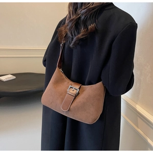 Close-up of brown suede hobo bag with leather strap and silver buckle detail on model