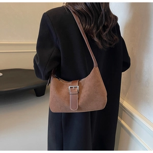 Detail of brown suede hobo bag with leather strap and silver metal buckle worn by a model
