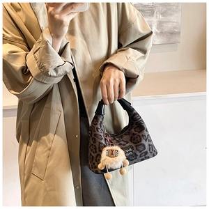 Detailed view of leopard print tote bag featuring black leather handles and plush charm