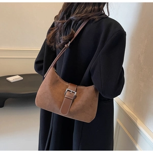 Detail of adjustable leather strap and metal buckle on brown suede shoulder bag