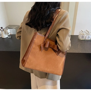 Detailed view of brown suede tote bag with large bow detail worn by a model