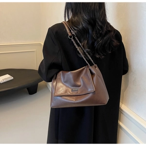 Braune Shopper-Tasche mit Metallkette und Logo-Plakette getragen von einem Model