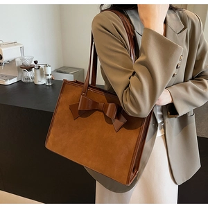 Close-up of brown suede tote bag featuring a large decorative leather bow detail