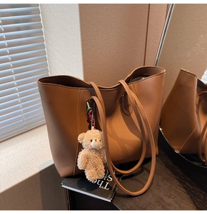 Detail view of large brown pebble leather tote bag with a cute plush bear charm on books