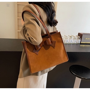 Brown suede tote bag with large bow detail shown on shoulder in a vintage interior