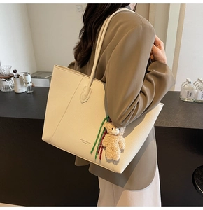 Detail of cream leather tote bag with teddy bear charm and fashion text print