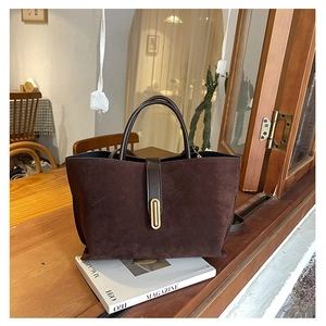 Detailed close-up of dark brown suede tote bag with golden oval buckle on a magazine