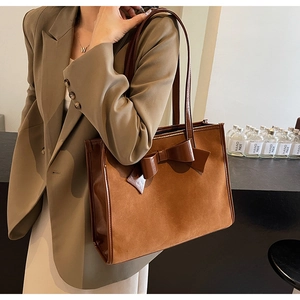 Detailed view of brown suede tote bag with large decorative bow and polished leather trim
