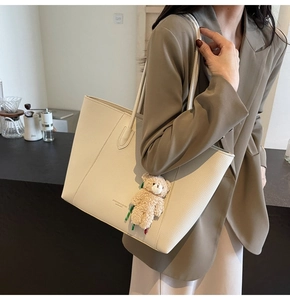 Detail of cream tote bag in lychee leather featuring a plush bear charm and fashion logo