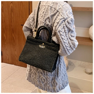 Model wearing black faux shearling tote bag with golden twist lock in home setting