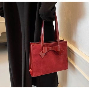 Close-up of suede and patent leather texture on a deep red tote bag with a bow