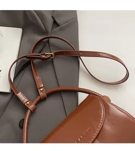 Detail of adjustable strap and circular handle on brown vintage glossy leather handbag