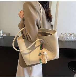 Close-up of beige lychee leather tote bag with a cute plush bear charm on strap