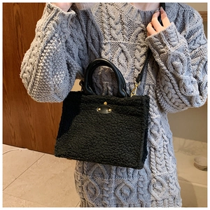 Detail der schwarzen Plüschtasche mit Ledergriff und Goldverschluss am Strickkleid