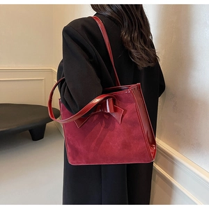 Detail of burgundy suede tote bag featuring a large bow and glossy patent leather panels