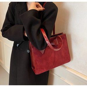 Detail view of large red tote bag with suede texture and glossy bow accent on wool coat
