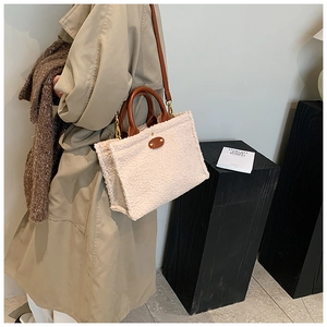 Detail der flauschigen cremefarbenen Plüsch-Tote-Bag mit braunen Ledergriffen und Goldbeschlag