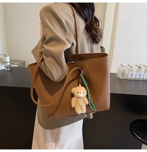 Detail of dark brown lychee leather tote bag with a cute plush bear charm accessory