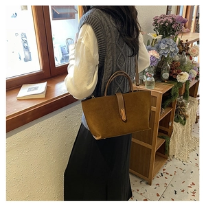 Brown suede tote bag shown on a model in a warm indoor scene with a crossbody strap