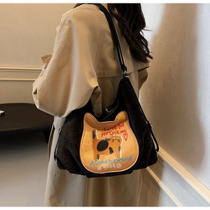 Close-up of black shoulder bag featuring a cartoon cat patch and artistic embroidery