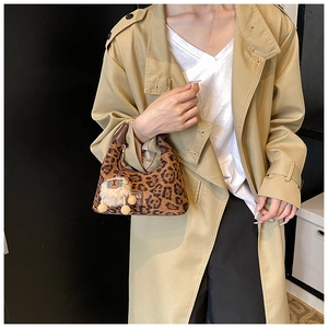 Detail view of leopard print handbag with plush sheep charm and brown handle on trench coat