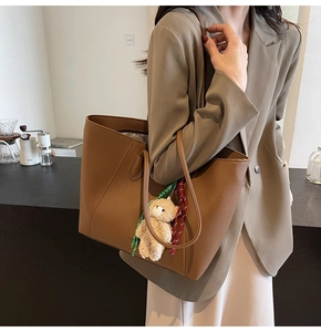 Brown large capacity leather tote bag with a plush bear charm worn on the shoulder